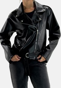 Veste de moto en similicuir noir avec taille ceinturée, fermeture éclair asymétrique et col à pression. Comprend deux poches avant et une texture lisse.