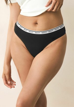 Chiloți tanga negri cu o talie elastică albă pe care este repetat numele brandului. Materialul este neted, cu un design ajustat și o acoperire minimă.