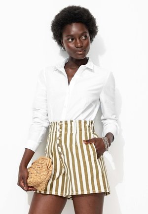 Chemise blanche à manches longues et short taille haute à rayures vert olive et blanches avec un devant à boutons. Tient une pochette texturée beige.