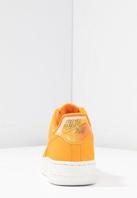 Baskets Nike Air orange avec un col rembourré, une semelle blanche et une tige texturée. Présente un logo bien visible sur le talon, design minimaliste.