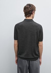 Polo shirt grigio a maniche corte con texture morbida e colletto, abbinato a pantaloni grigi chiari. Il retro mostra cuciture lisce e una silhouette aderente.