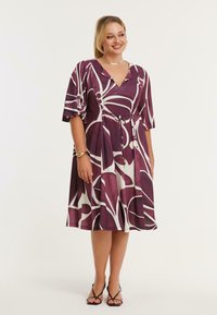 Lilla og hvid blomsterprintkjole, knælang, med V-hals, korte ærmer, bindebånd i taljen, flydende tekstur og en afsluttet nedringning med vidde.