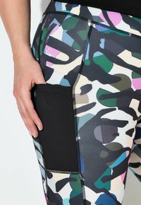 Close-up van een hand die in de zwarte gaas zijzak van multikleurige abstracte patroonleggings steekt.