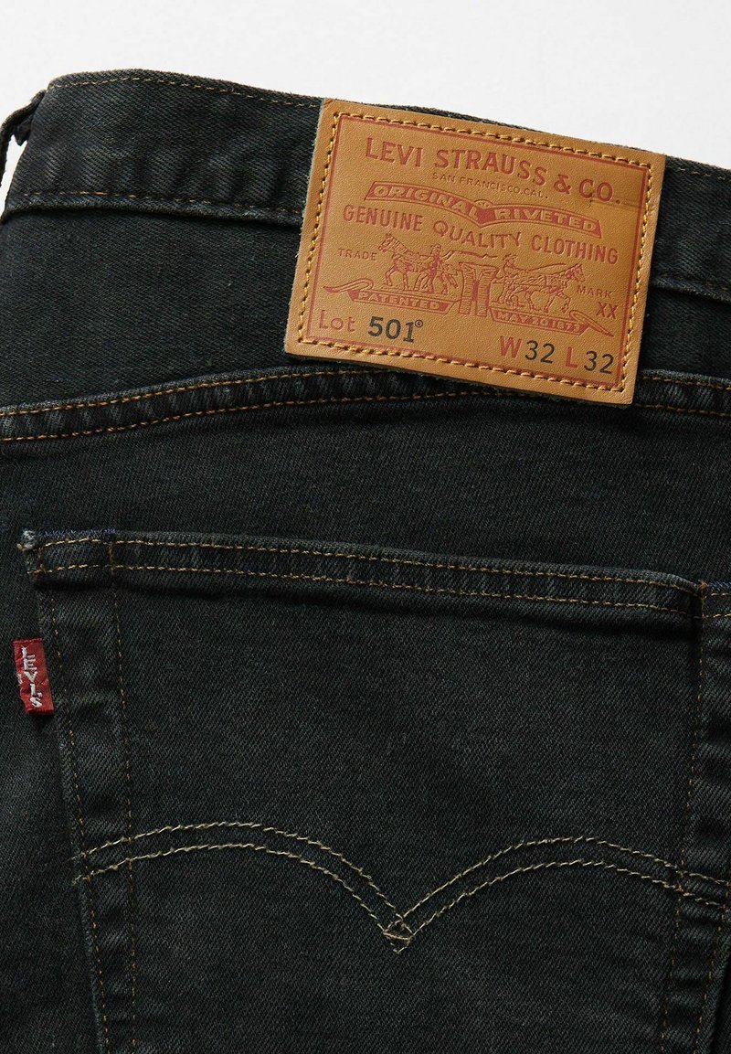 Zwarte Levi's 501-jeans met zichtbare achterzak, tan leren merklabel met maat W32 L32 en een rode Levi's stoffen label.