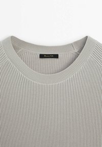 Pull en maille gris côtelée avec un col rond et une étiquette noire au col. Le tissu a une finition texturée avec des lignes verticales.
