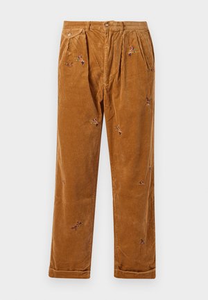 Pantalones de pana marrones con delicados bordados florales, que cuentan con un ajuste relajado, pliegues frontales visibles y detalles de dobladillo enrollado.