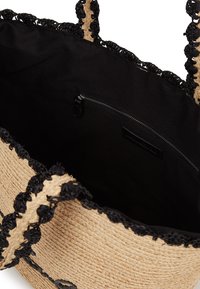 Austo pītā salmu soma ar dabīgu krāsu un melnu viļņu apdari, kas iekļauj melnu auduma iekšpusi un kabatu ar rāvējslēdzēju.