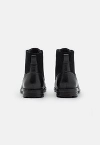 Paire de bottines en cuir et suède noir vues de dos sur un fond blanc.