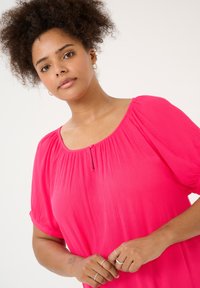 Blusa di un vivace rosa con colletto rotondo, texture arricciata e maniche a sbuffo corte. Presenta un piccolo bottone sul colletto.