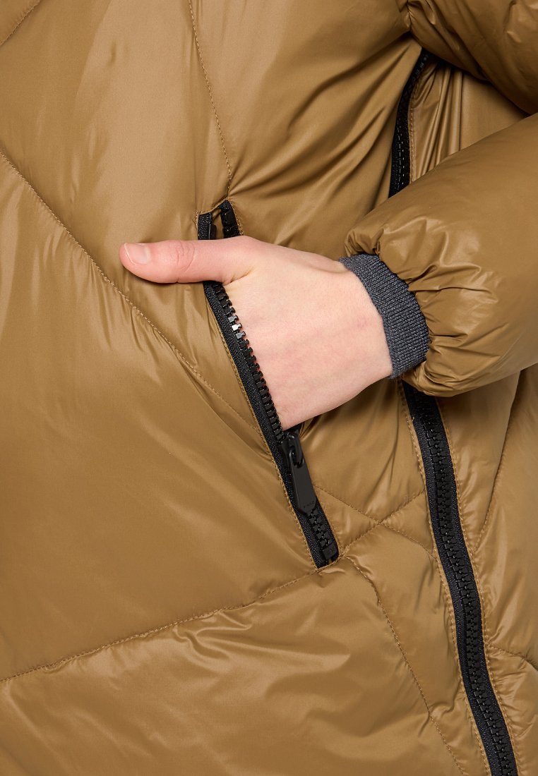 Hand in einer braunen gesteppte Jackentasche mit schwarzem Reißverschluss, grauer Bund am Handgelenk sichtbar.