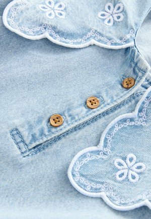 Heled sinine denim kangas, millel on lainelised servad, valged tikandid, dekoratiivsed lillemustrid ja puidust nupud.