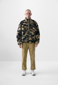 Fleece pullover with a high collar, featuring a brown and black floral pattern; paired with khaki pants and white sneakers.