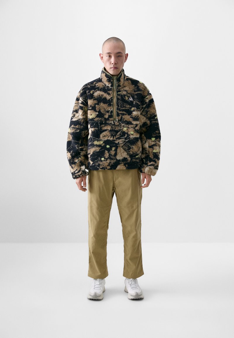 Fleece pullover with a high collar, featuring a brown and black floral pattern; paired with khaki pants and white sneakers.