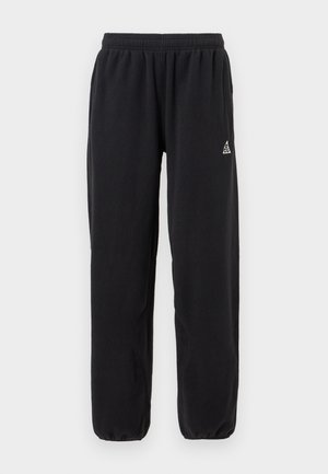 Svarte joggebukser laget av mykt stoff, med elastisk midjebånd og innsnevring ved leggen. Lite logodesign nær midjebåndet.