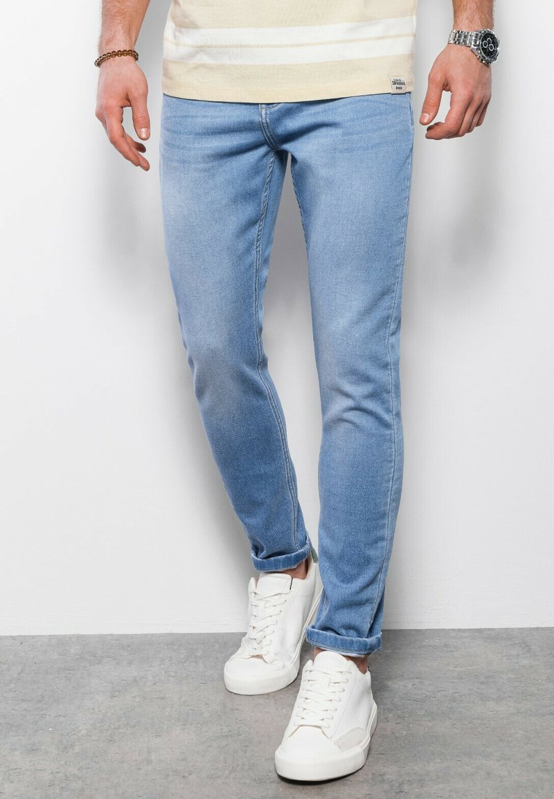 Vaqueros ajustados de denim en un tono azul claro, con un diseño clásico de cinco bolsillos. Combinados con zapatillas blancas, mostrando líneas limpias y un detalle minimalista.