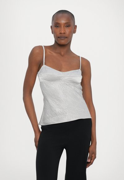 Top sin mangas plateado con un acabado texturizado, que presenta un escote ligeramente curvado y tirantes finos, combinado con pantalones negros.