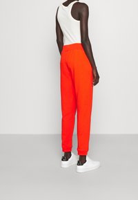 Röda träningsoverallsbyxor med elastisk midja och avslutade anklar, i kombination med en vit linne och vita sneakers med svarta accenter.