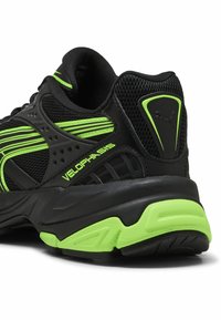 Deportiva negra con acentos en verde neón, que presenta una parte superior de malla, lados texturizados y una suela acolchada. Marca "Velophasis" en el costado.