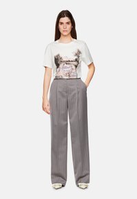 Witte T-shirt met een landschapsgrafiek, gecombineerd met hooggewijd grijs gestreepte broek. De schoenen hebben lichte, ronde accenten.