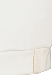 Weißer Sweater aus weichem Material, mit einem gerippten Saum und einem gestickten Logolabel in einer hellen Nuance nahe dem unteren Ende.