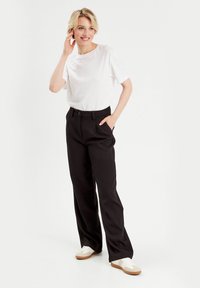 T-shirt blanc à manches courtes associé à un pantalon noir taille haute ; le pantalon présente des poches latérales et une texture lisse et structurée.