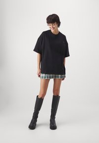 Camiseta negra de gran tamaño con mangas cortas, combinada con una mini falda de cuadros verdes y botas de cuero negras hasta la rodilla con un acabado texturizado.