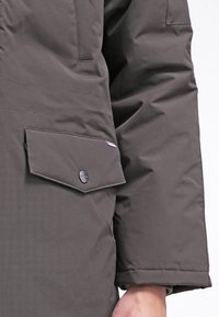 Giubbotto imbottito grigio scuro con tasca a chiusura a scatto, texture trapuntata e finitura liscia su corpo e maniche.
