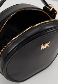 Černá kožená kulatá kabelka se zlatým zipem a logem. Vnitřek je z černé látky, nabízí dostatek prostoru a hladkou strukturu.