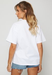 Camiseta de algodón blanca con un corte relajado y mangas cortas, con un clásico escote redondo. Combinada con pantalones cortos de mezclilla desgastados.