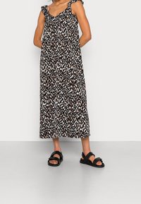 Dlouhá maxi šaty s černobílým a hnědým vzorem a volánkovými ramínky; doplněné černými nazouvacími sandály s širokým páskem a sponou.