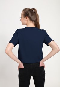 Námořnická modrá tričko vyrobené z měkké tkaniny, s krátkým rukávem a volným střihem, v kombinaci s černými džíny, pohled zezadu.