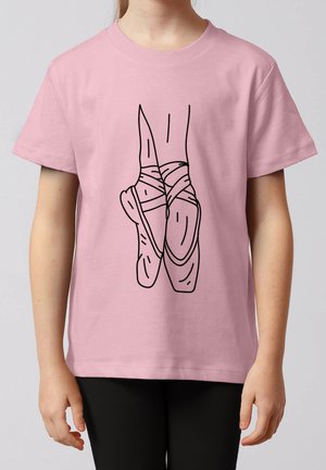 Enfant portant un t-shirt rose avec un dessin en ligne noire représentant des pieds de ballet croisés en pointes sur le devant.