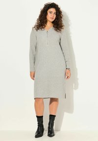 Abito grigio a costine con collo zip, maniche lunghe e fessure laterali. Abbinato a stivali neri alla caviglia con dettagli decorativi.