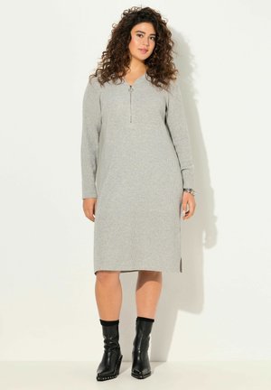 Graues, geripptes Kleid mit Reißverschluss am Hals, langen Ärmeln und Seitenschlitzen. Kombiniert mit schwarzen Knöchelstiefeln mit dekorativen Akzenten.