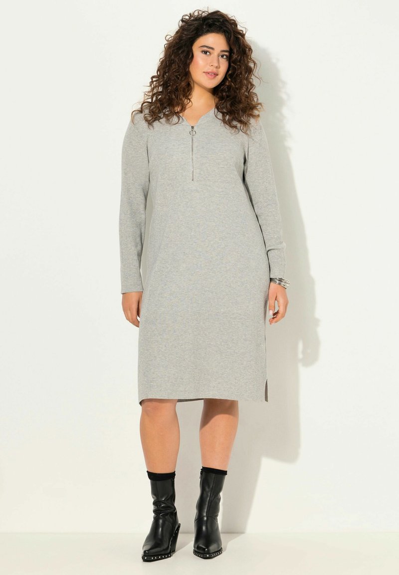 Abito grigio a costine con collo zip, maniche lunghe e fessure laterali. Abbinato a stivali neri alla caviglia con dettagli decorativi.
