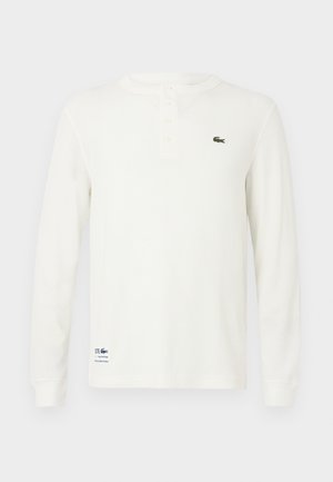 Witte lange mouwen henley shirt van een gestructureerde ribstof, met een drie-knopen pat en een groen geborduurd krokodillenlogo op de borst.