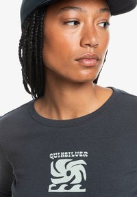 Dark gray ribbed t-shirt featuring a light green Quiksilver logo design. Soft texture with a round neckline and fitted silhouette.