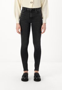 Augsti vidukļa melnie džinsu skinny džinsi ar gludu tekstūru un minimālu nodilumu, kombinēti ar melnajiem loafers.