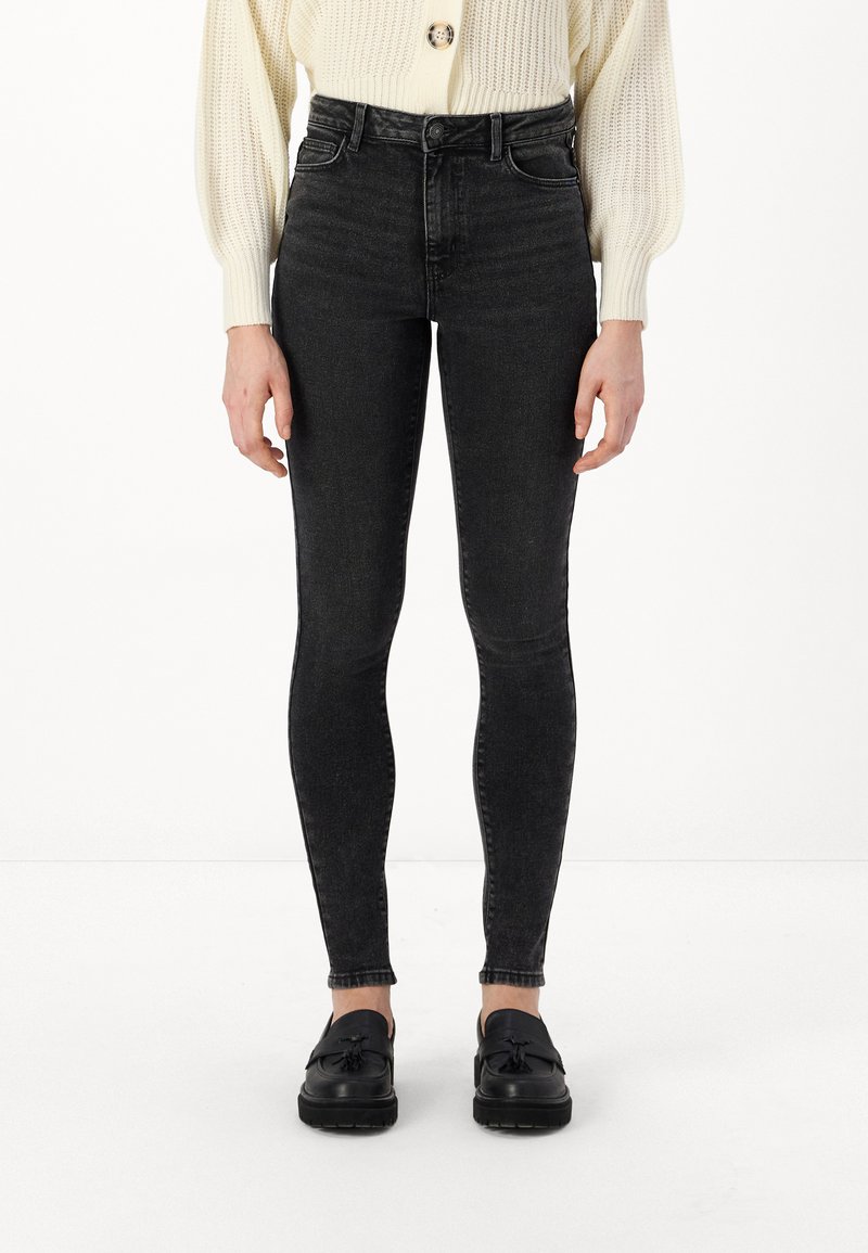 Augsti vidukļa melnie džinsu skinny džinsi ar gludu tekstūru un minimālu nodilumu, kombinēti ar melnajiem loafers.