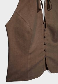 Gilet marron sans manches avec des boutons recouverts de tissu sur le devant et une encolure en V subtile, présenté sur un fond uni.