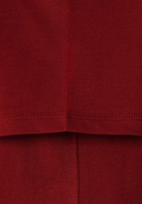 Červená ribbed tkanina se dvěma vrstvami, viditelné švy na lemu a švech naznačují měkkou texturu a pružný design.