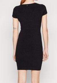 Robe bodycon noire côtelée avec des manches courtes et une silhouette ajustée. Elle présente un discret détail de bouton à l'arrière et une texture lisse.