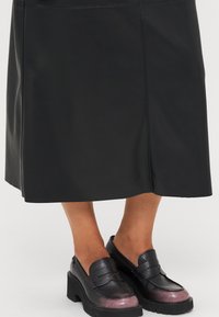 Fekete bőr szoknya egyenes fazonnal, tiszta vonalakkal. Fekete és fém rózsaszín, vastag talpú lakkcipővel párosítva.