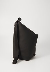 Svart skinn skulderveske med minimalistisk, asymmetrisk design. Har en solid tekstilrem og en glatt matt overflate.