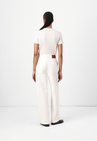Light-colored t-shirt with subtle pattern, paired with wide-leg white trousers featuring back pockets and a brown leather patch. Black shoes.
