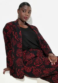 Blazer a kalhoty s černým a červeným květinovým vzorem a texturovaným povrchem. Blazer má klopený límec a dlouhé rukávy.