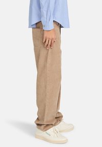 Khaki corduroy pants with a straight-leg design, featuring side pockets and a textured finish, paired with white sneakers.