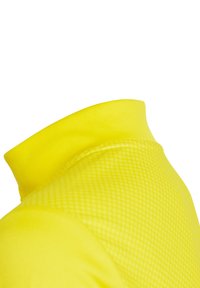 Maglietta sportiva gialla con colletto alto e pannello in rete testurizzata, progettata per traspirabilità e comfort.