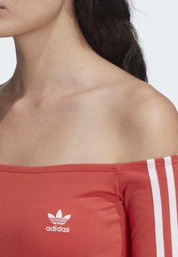 Rode off-the-shoulder top met witte drie-stripes accenten en geborduurd logo; gladde stof en aangesloten ontwerp.