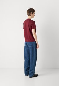 Burgunderfarget T-skjorte med korte ermer kombinert med løstsittende, lyseblå denimjeans. Jeansen har baklommer og en avslappet silhuett.